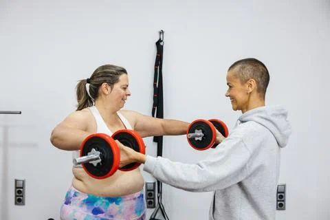 Personal trainer helping client with shoulder and back training using dumbbells Stock Photos