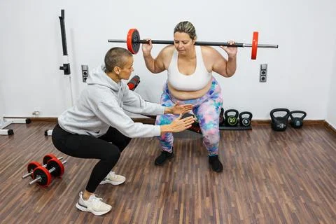 Personal trainer helping client with weight squat training in gym Stock-Fotos