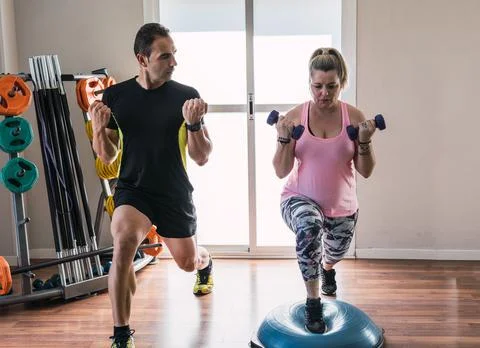 Personal trainer helping to do a weight exercise to a woman indoors Stock Photos