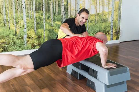 Personal trainer helping a man do push-ups indoors Stock Photos