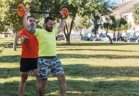 Personal trainer helping a man to do weights outdoors Stock Photos