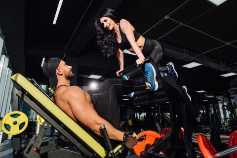 Personal trainer helping a men working out on leg press machine in gym Stock Photos