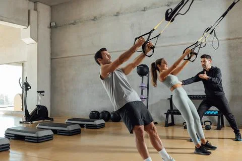 Personal trainer helps a couple that work out with elastic resistant strap. Stock Photos