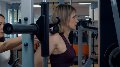 Personal trainer helps to work out in the gym. A woman pumps up the muscles of Stock Photos