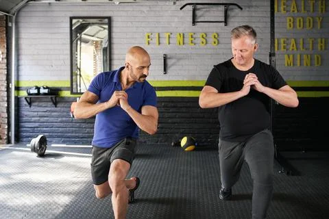 Personal trainer instructing senior man, leg lunges exercise Stock Photos