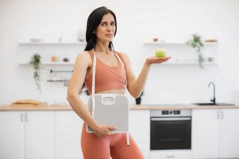 Personal trainer posing with apple and weight scales indoors 库存照片