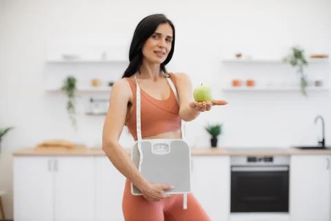Personal trainer posing with apple and weight scales indoors Stock Photos
