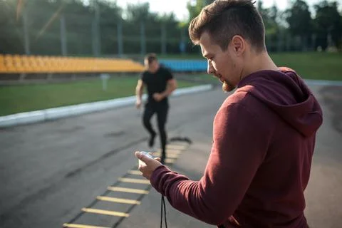Personal trainer with stopwatch measuring time of male exercising outdoor Stock-Fotos