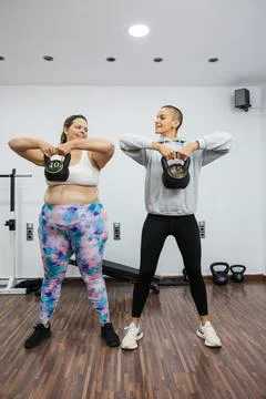 Personal trainer supporting overweight client lifting kettlebells in gym Stock Photos