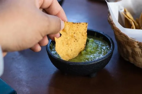 Personal view of hand putting corn chips in green spicy sauce 库存照片