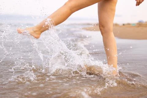 Person's bare legs creating a refreshing splash in the shallow ocean water,.. Stock Photos