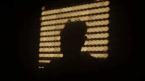 Person's dark silhouette standing in front of a golden bokeh pattern on a black Stock Footage 343535889