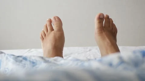 Person's feet sticking out from under blue patterned blanket on bed. Stock Footage 332626947