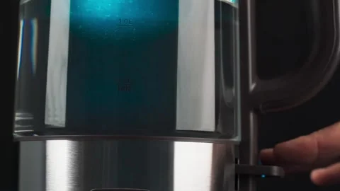 A person's fingers press the button of a glass kettle to boil water. Bubbles are Stock Footage 167775050