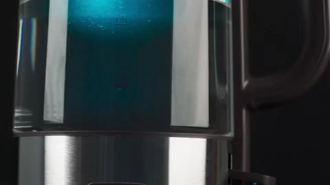 A person's fingers press the button of a glass kettle to boil water. Bubbles are Stock Footage 168235100