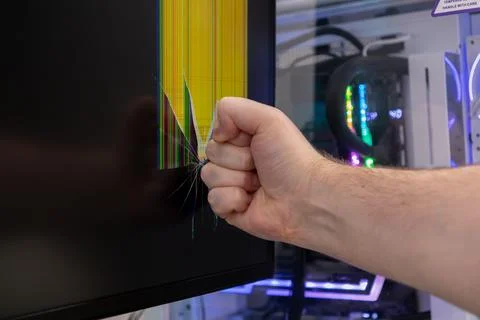 A person's forceful fist impacts a computer monitor, shattering the display.. 库存照片