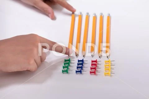 Person's Hand Arranging Pencils And Multi Colored Pushpins Stock Photos