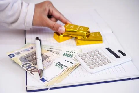A person's hand arranging three fine gold bars on an open notebook next to .. Stock Photos