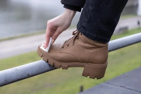 Person's hand cleaning a brown combat boot with a wet wipe on an outdoor ra.. Stock Photos