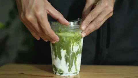 Person's hand closes the lid on a plastic cup with iced Matcha green tea. Stock Footage 263342341