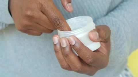 Person's hand dipping finger into a small white jar of cream or ointment. Vidéo 333031212
