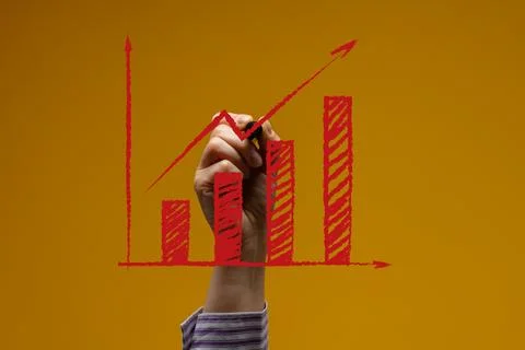 A person's hand draws a red bar graph with an upward arrow on a yellow back.. Stock Photos