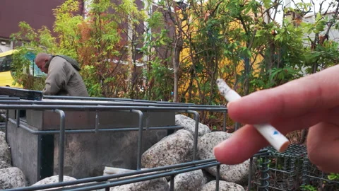 Person's hand holding a burning cigarette in a tokyo urban park setting Stock-Footage 330297634