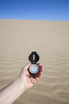 A persons hand holding a navigation compass against the backdrop of a sandy.. Stock Photos