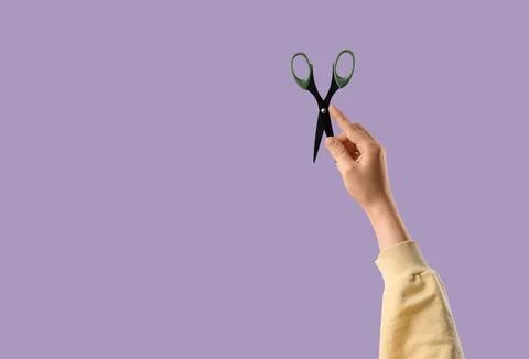 Persons hand holding open black and green scissors against a solid purple bac Stock Photos