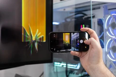 Person's hand holds a smartphone capturing a shattered computer monitor scr.. 스톡 사진