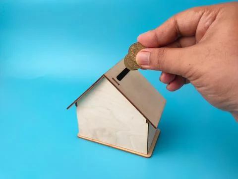 A person's hand inserts two gold coins into the roof slot of a small wooden.. Stock Photos