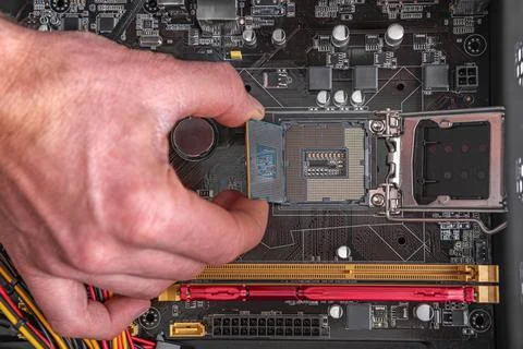A persons hand installs a central processing unit into the socket of a modern Stock Photos