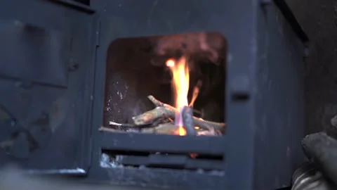 A persons hand loading sticks onto a wood-burning stove fire Stock Footage 150680955