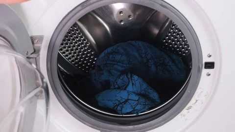 A persons hand places laundry in the drum of a washing machine 库存影片 316256800