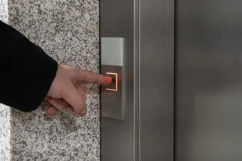 A person's hand presses an illuminated elevator button on a stainless steel.. Foto stock