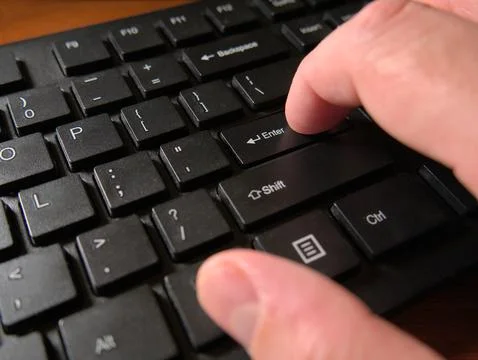 A person's hand pressing the Enter key on a black computer keyboard Stock Photos