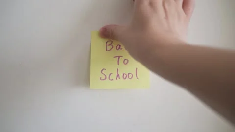 A person's hand pressing a square yellow sticky note onto a plain white wall. Stock Footage 344514446