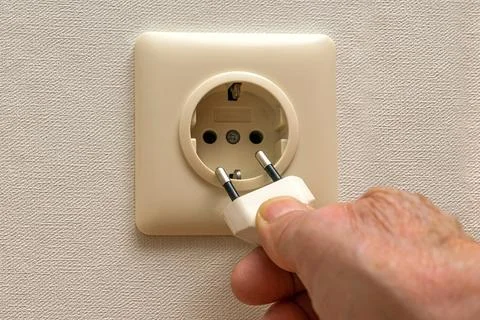 A person's hand pulls the plug out of an electrical outlet. Stock Photos