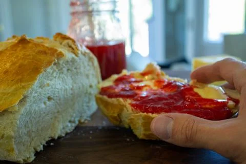 Persons hand reaching for a slice of bread with fresh jam and butter. Foto stock