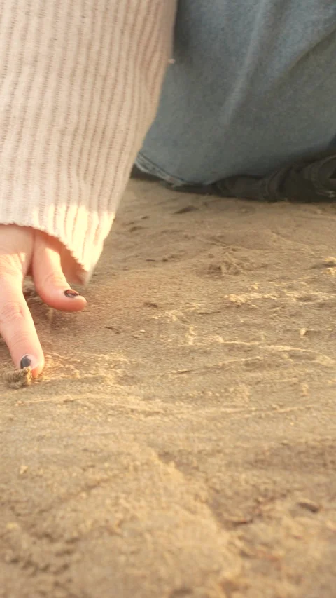 A person's hand is on the sand, with a black and yellow nail polish design Stock Footage 276436059