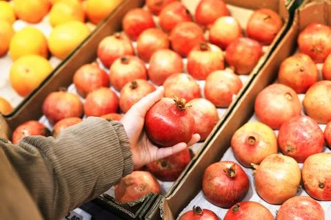 A person's hand selects a ripe, red pomegranate from a display box, with bl.. Stock Photos