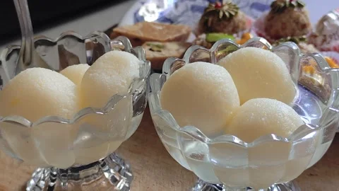 Persons hand taking Indian sweet Rasgulla from transparent glass bowl filled Vidéo 321307063