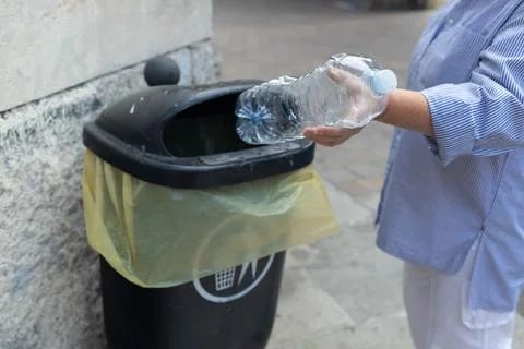 Person's hand throwing an empty transparent plastic water bottle into a black pu Stock Photos
