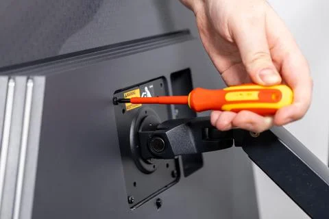 Persons hand using a bright orange screwdriver to secure a computer monitor.. Stock Photos