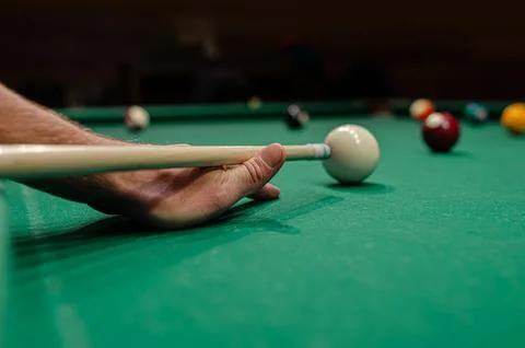 A persons hand using a cue stick to aim at a white cue ball on a felt pool table Stock Photos