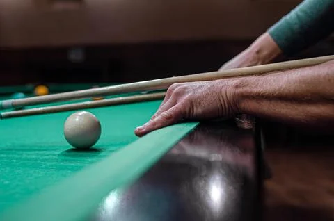 A persons hand using a cue stick to aim at a white cue ball on a felt pool table Stock Photos