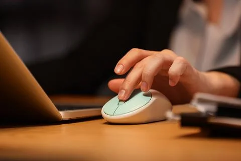 Persons hand using a mint green computer mouse on a wooden desk next to a lap Stock Photos