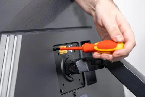 Person's hand using a red and yellow screwdriver to secure a screw on a mon.. Stock Photos
