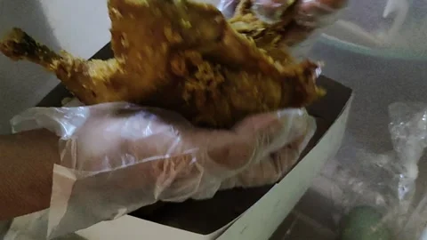 Person's hand wearing a transparent plastic glove cutting up fried chicken Stock Footage 296166642