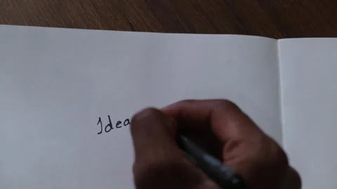 Person's hand writing the word "Ideas" with a black pen on a blank white paper 動画素材 330480267